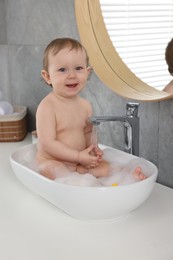 Photo of Cute little baby bathing in sink at home