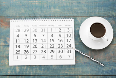 Photo of Flat lay composition with calendar and cup of coffee on light blue wooden table