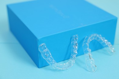 Photo of Transparent dental aligners on light blue background, closeup