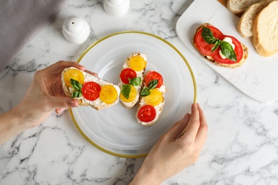 Photo of Woman eating tasty fresh tomato bruschettas at marble table, flat lay