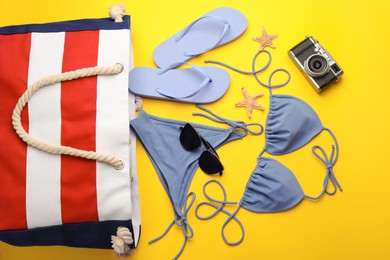 Photo of Stylish bag with beach accessories on yellow background, flat lay