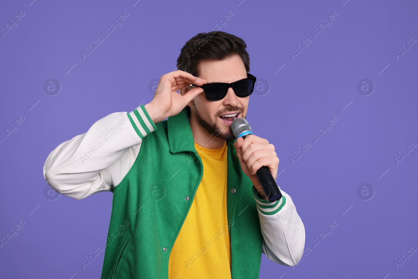 Photo of |Handsome man with sunglasses and microphone singing on purple background