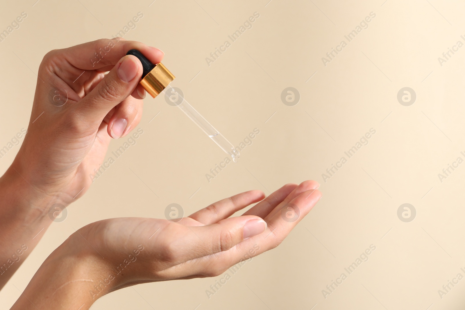 Photo of Woman applying cosmetic serum onto her finger on beige background, closeup. Space for text