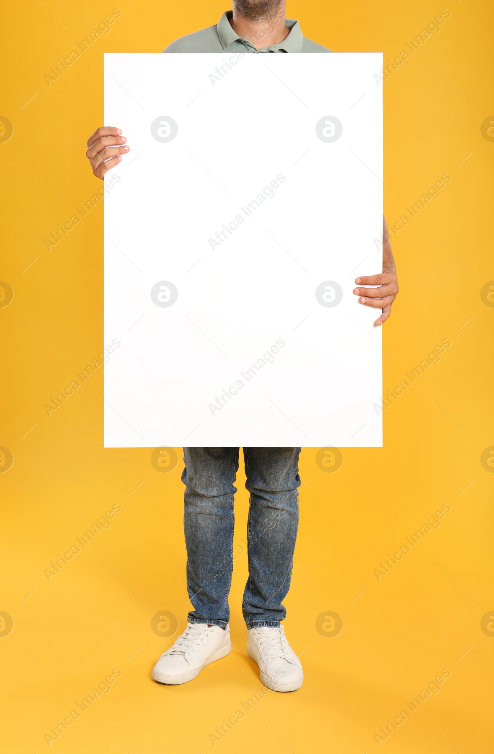 Photo of Man holding white blank poster on yellow background, closeup. Mockup for design