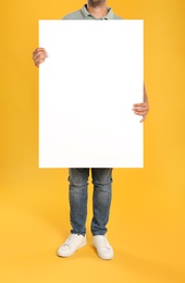 Photo of Man holding white blank poster on yellow background, closeup. Mockup for design