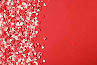 Photo of Bright heart shaped sprinkles on red background, flat lay. Space for text
