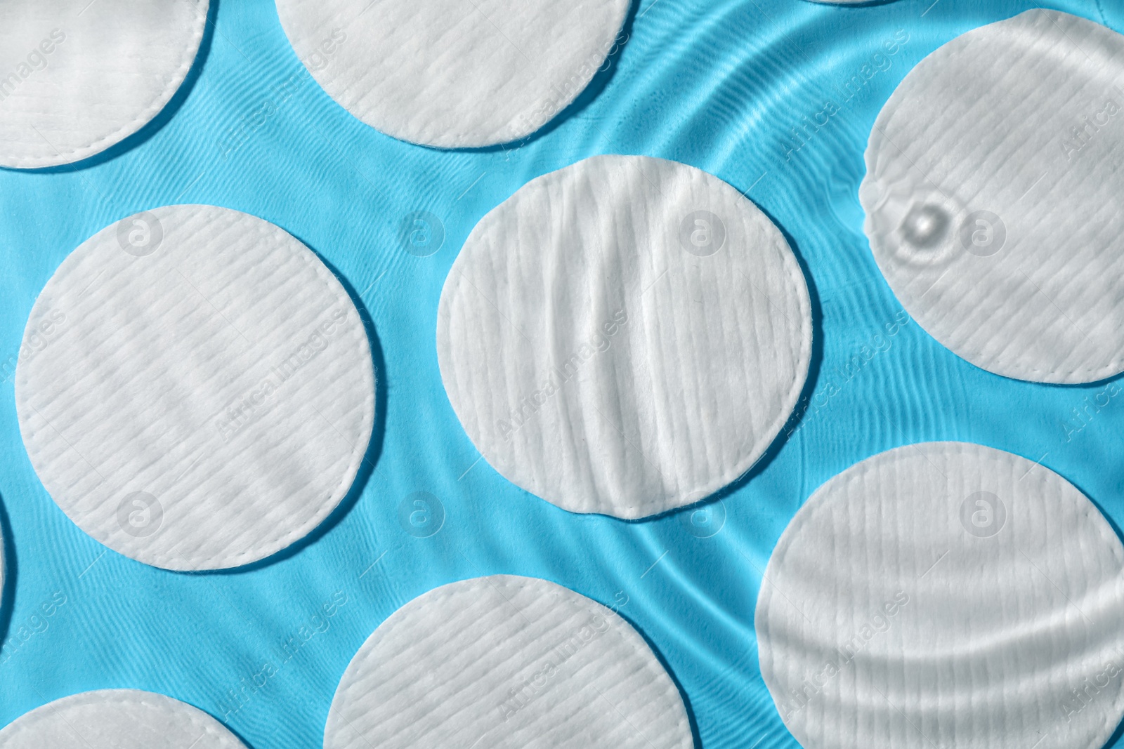 Photo of Many cotton pads in water on light blue background, flat lay