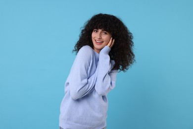 Happy young woman in stylish warm sweater on light blue background