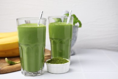 Glasses of tasty matcha smoothie and powder on white table, space for text