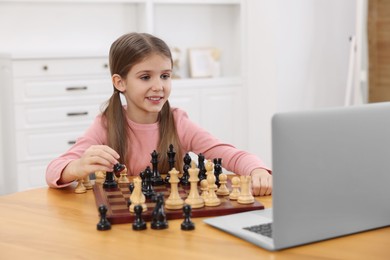Cute girl learning to play chess with online tutor at home