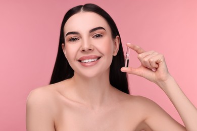 Photo of Beautiful young woman holding skincare ampoule on pink background