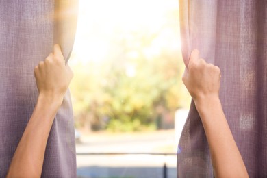 Image of Woman opening curtains in sunlit room, closeup