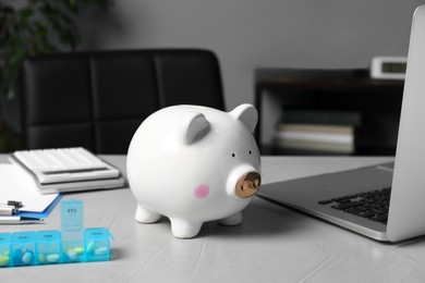 Photo of Piggy bank near pills and laptop on table in hospital. Medical insurance