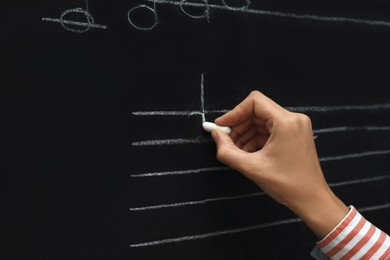 Photo of Teacher writing music notes with chalk on blackboard, closeup