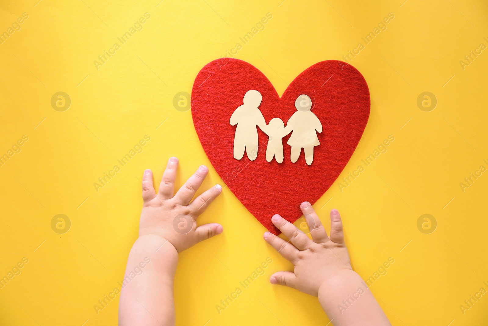 Photo of Little child's hands near red heart and paper silhouette of people on color background, top view