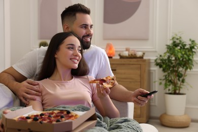 Photo of Happy young couple watching tv and eating pizza on sofa in living room. Space for text