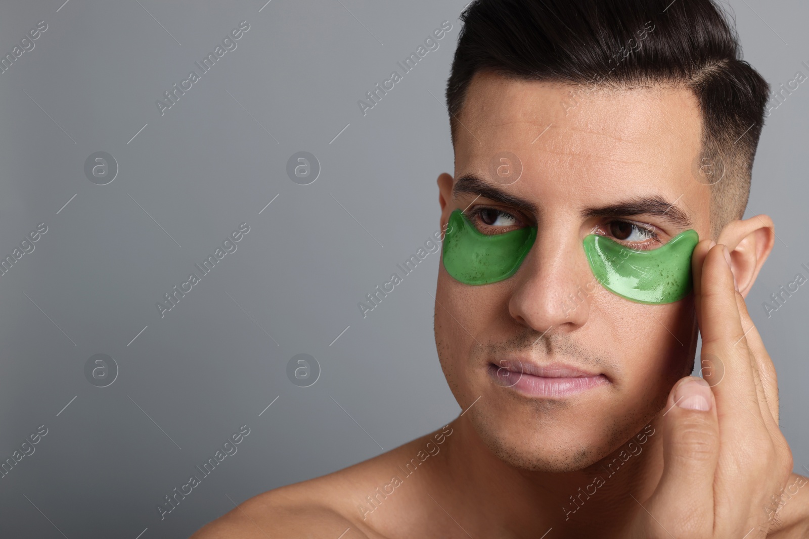 Photo of Man applying green under eye patch on grey background. Space for text