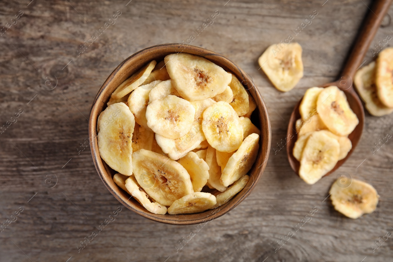 Photo of Bowl and spoon with sweet banana slices on wooden table, top view. Dried fruit as healthy snack