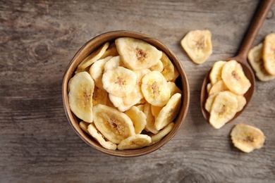 Photo of Bowl and spoon with sweet banana slices on wooden table, top view. Dried fruit as healthy snack
