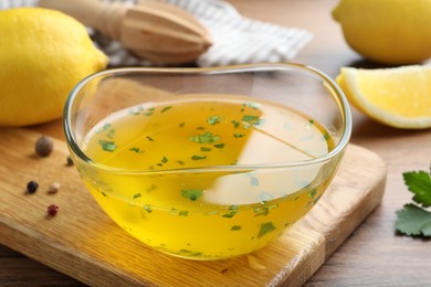 Photo of Bowl with lemon sauce and ingredients on wooden table, closeup. Delicious salad dressing