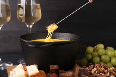 Dipping piece of bread into fondue pot with melted cheese on table, closeup