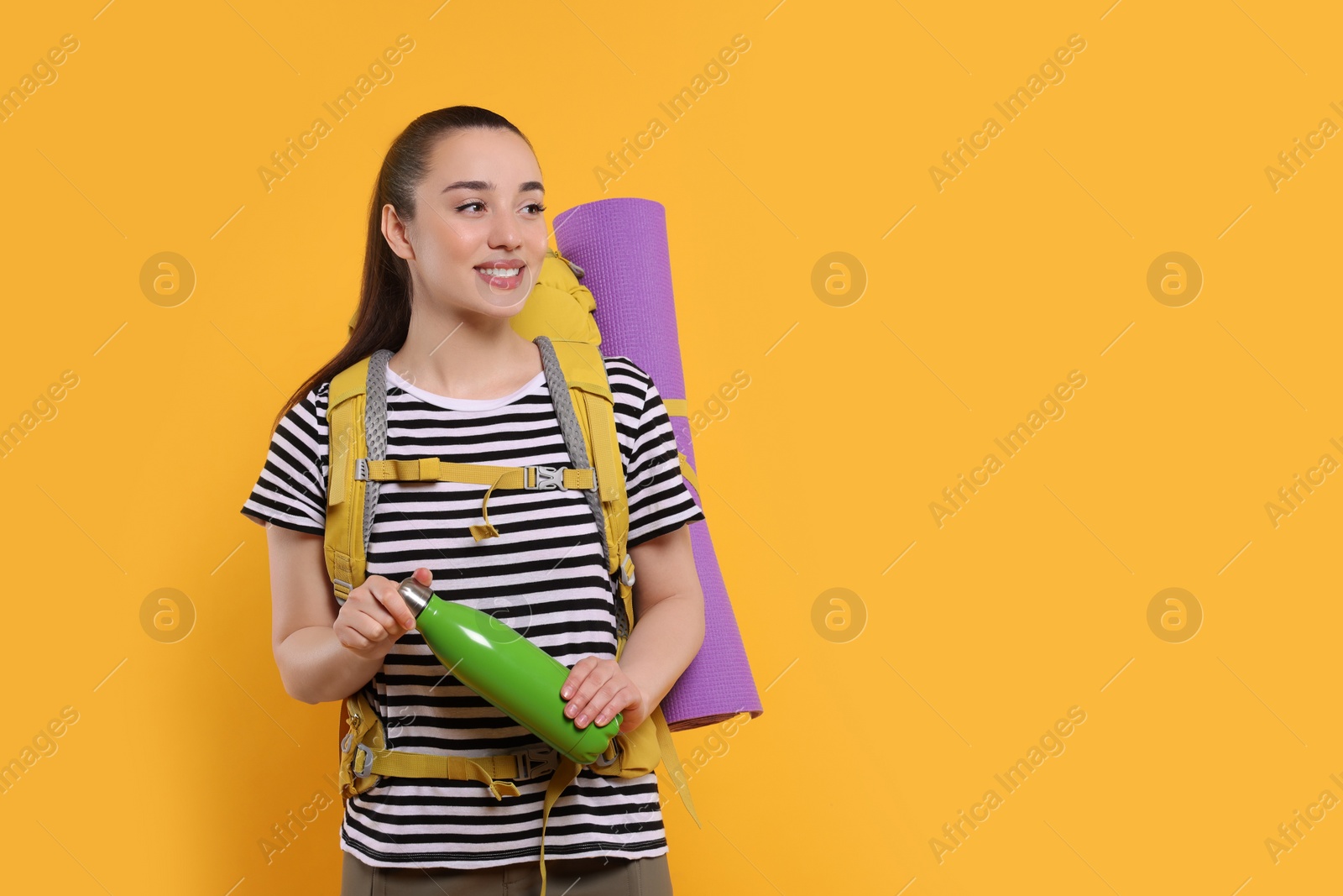 Photo of Smiling young woman with backpack and thermo bottle on orange background, space for text. Active tourism