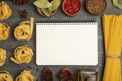 Photo of Blank recipe book, spices and raw pasta on dark grey table, flat lay. Space for text