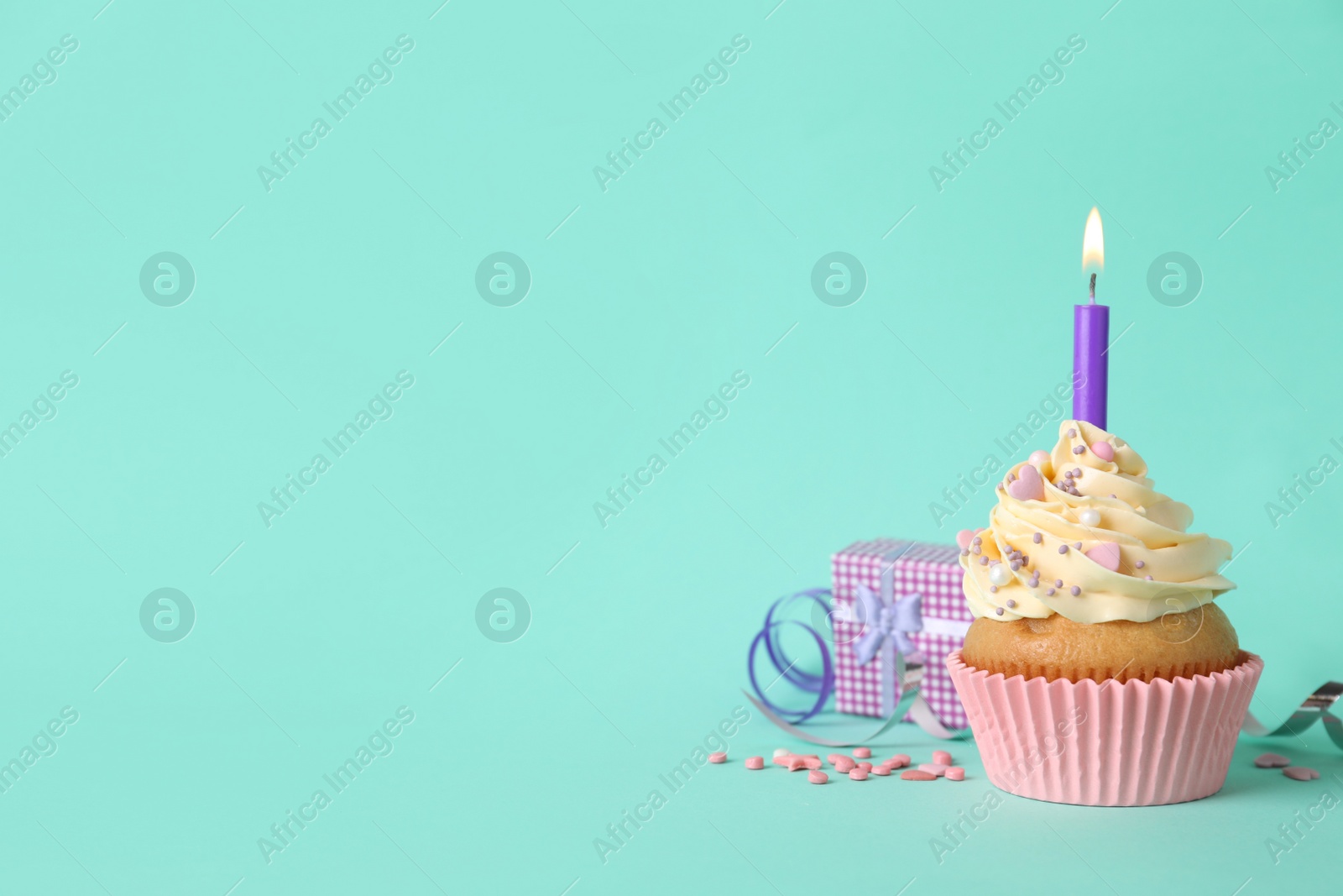 Photo of Birthday cupcake with burning candle, gift box  and sprinkles on turquoise background. space for text