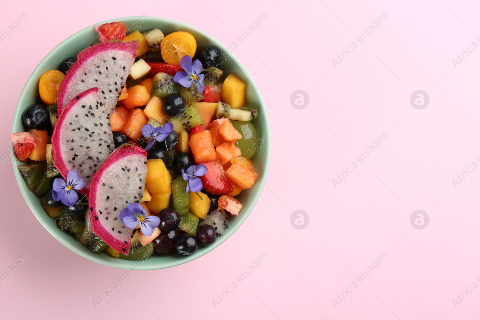 Photo of Delicious exotic fruit salad on pink background, top view. Space for text