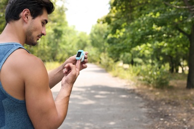 Young man checking pulse with medical device after training in park. Space for text