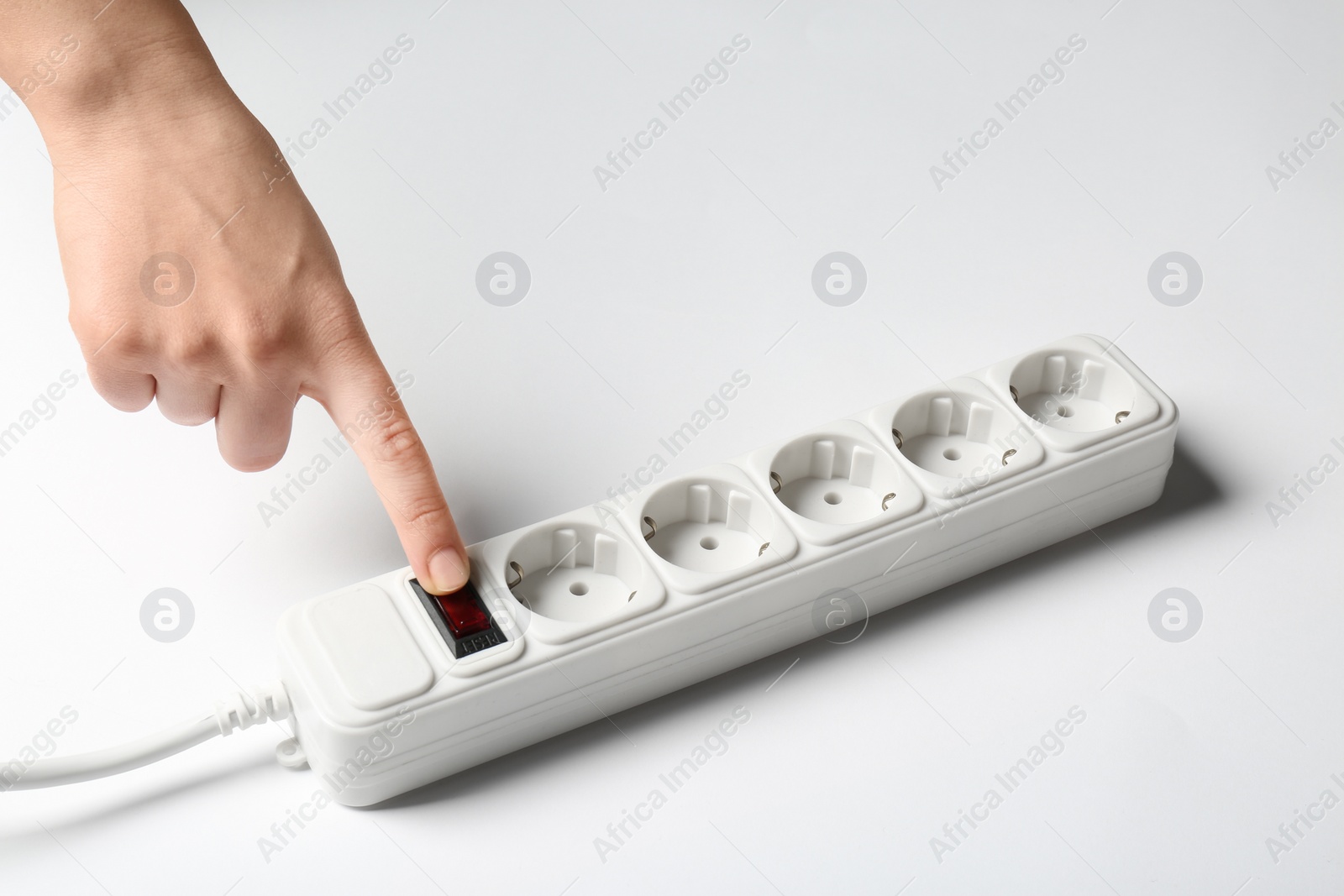 Photo of Woman pressing power button of extension cord on white background, closeup. Electrician's equipment