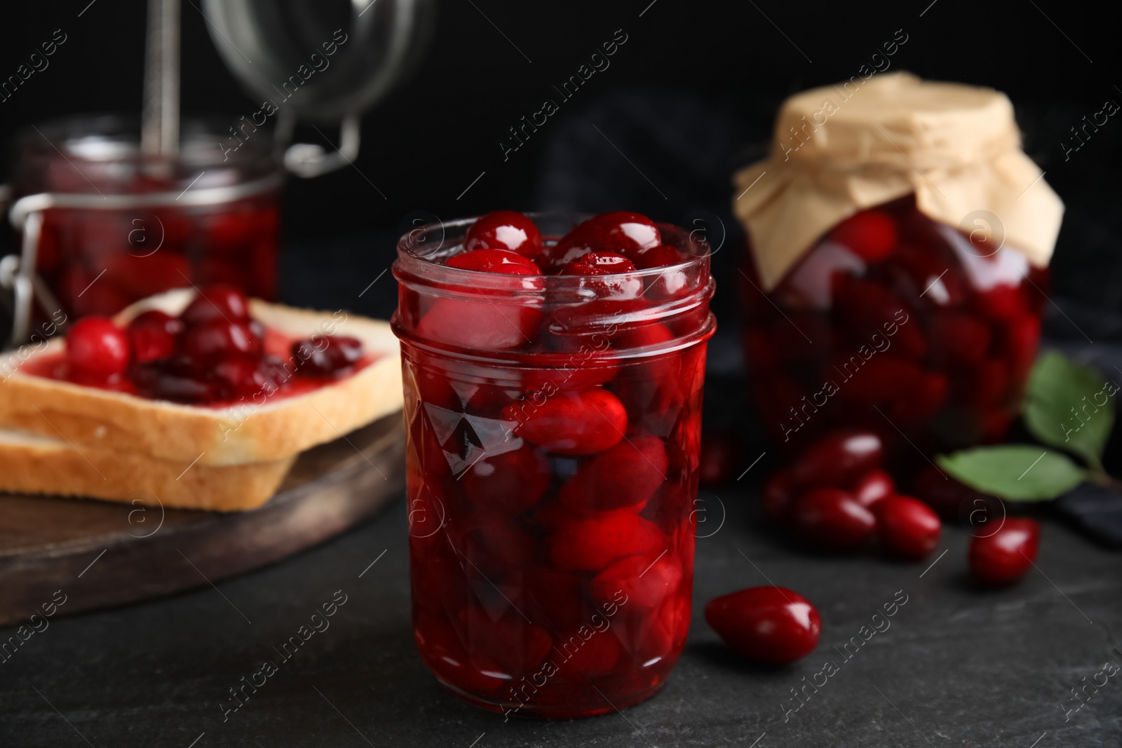 Photo of Delicious dogwood jam with berries in glass jar on black table
