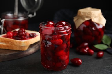 Photo of Delicious dogwood jam with berries in glass jar on black table