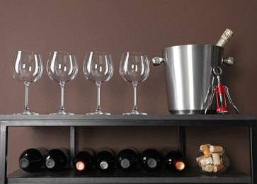 Photo of Glasses, bucket, corkscrew and bottles of wine on rack near brown wall