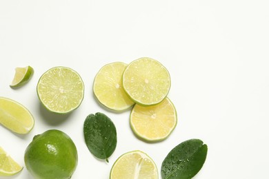 Photo of Whole and cut fresh ripe limes with green leaves on white background, flat lay