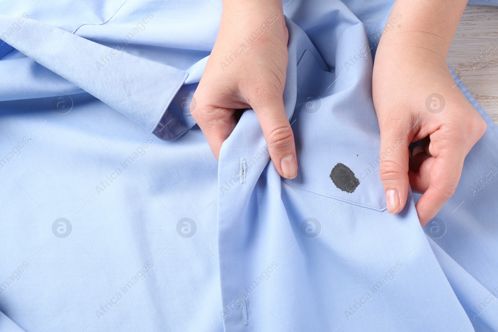 Photo of Woman holding shirt with black ink stain, top view
