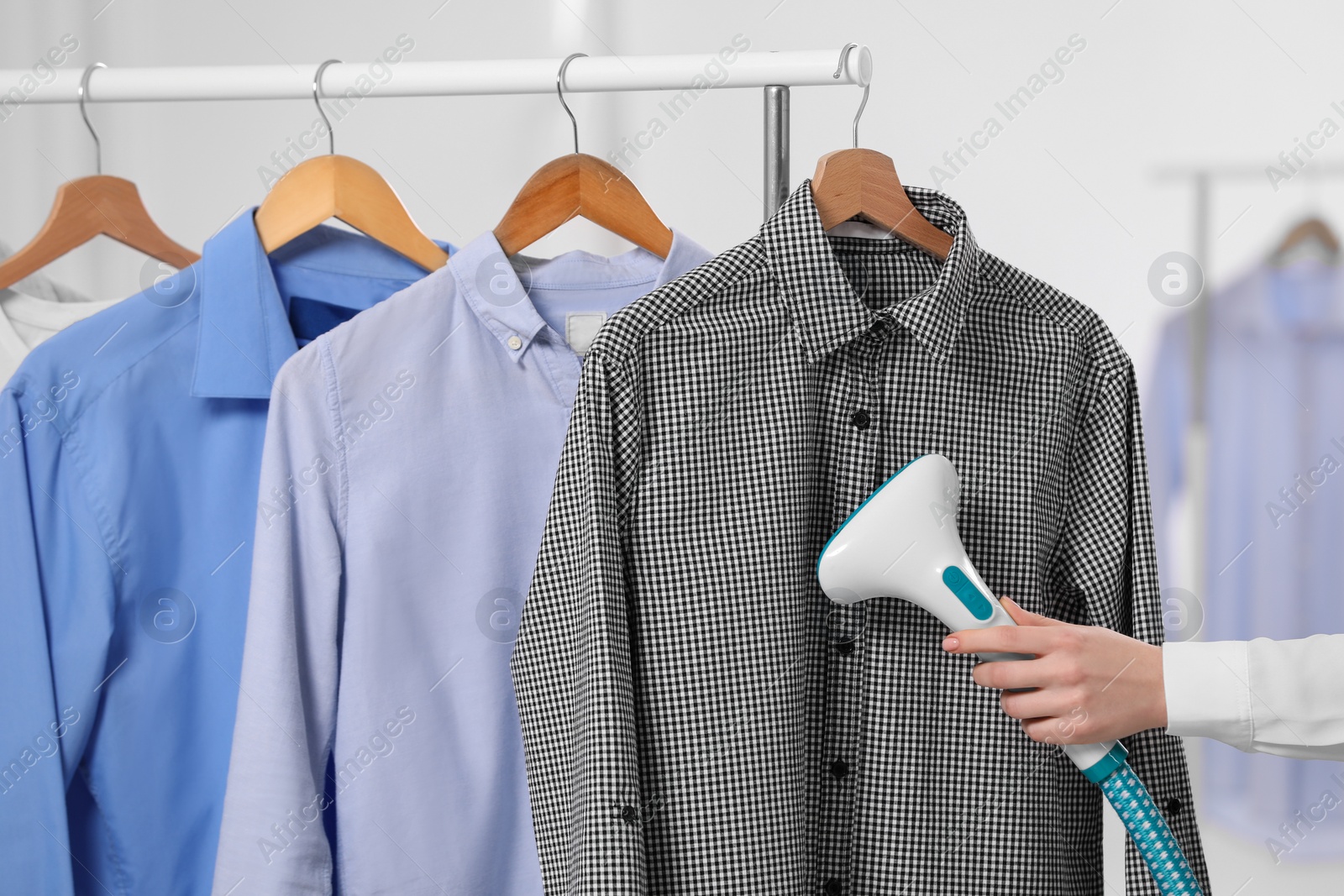 Photo of Woman steaming shirt on hanger in room, closeup