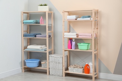 Wooden shelving units with clean towels and detergents in stylish room interior