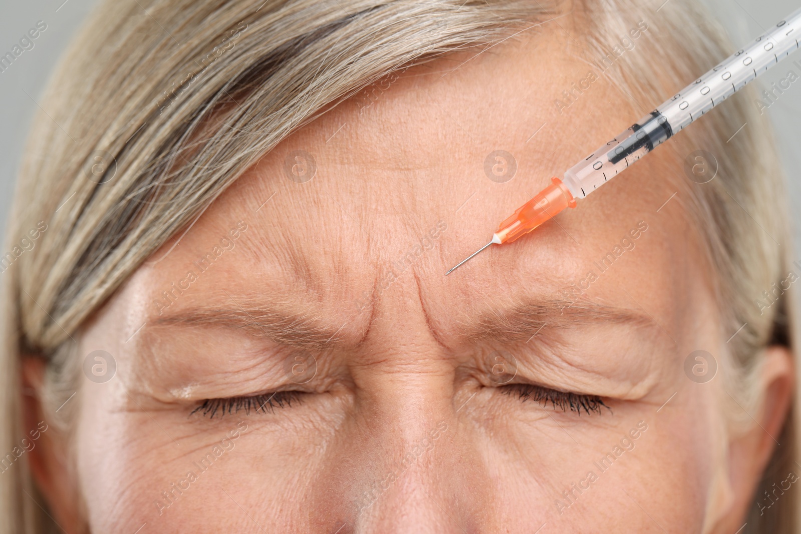 Photo of Senior woman getting facial injection on light grey background, closeup. Cosmetic surgery