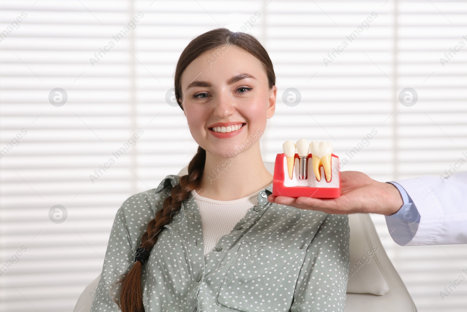 Photo of Doctor with educational model of dental implant consulting patient in clinic