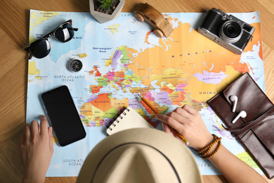 Woman with notebook and world map planning trip at wooden table, top view