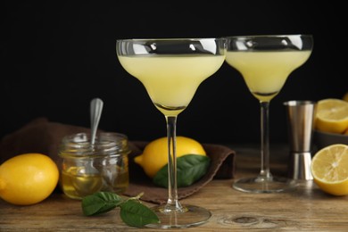 Photo of Delicious bee's knees cocktails and ingredients on wooden table against dark background