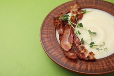 Photo of Delicious potato soup with bacon and microgreens in bowl on green table, closeup. Space for text