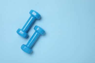 Photo of Two dumbbells on light blue background, top view. Space for text