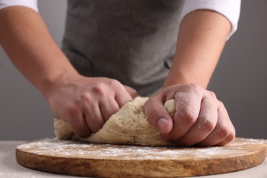 Photo of Man kneading dough at table near grey wall, closeup