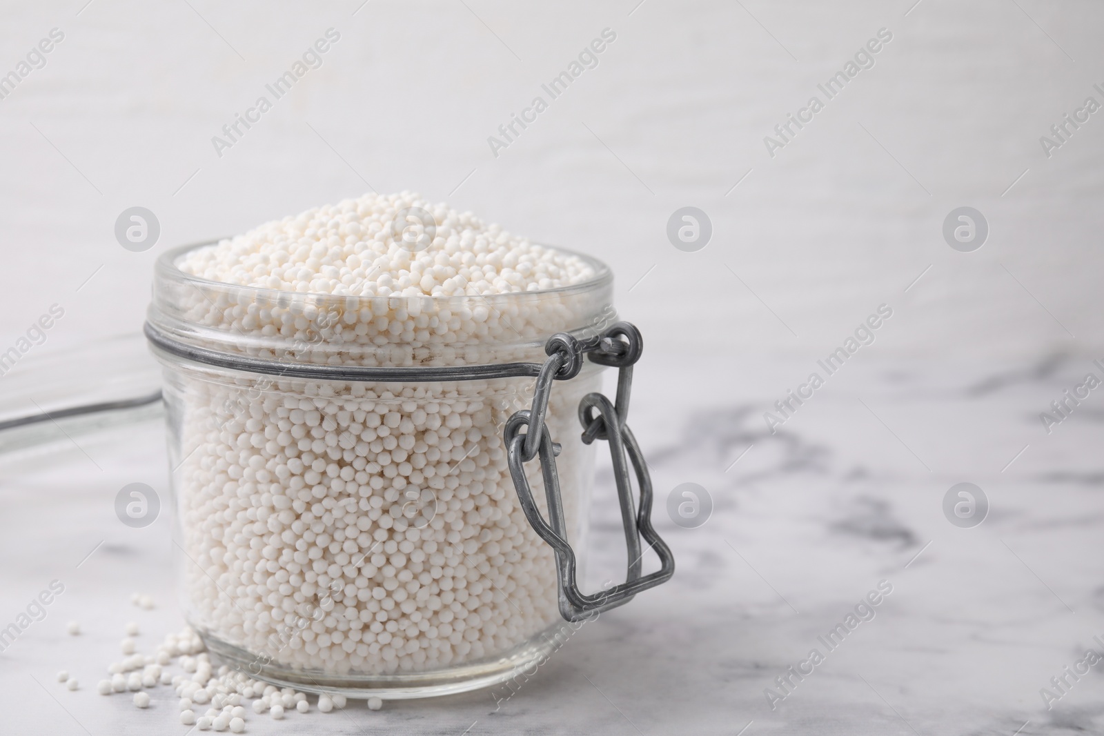 Photo of Tapioca pearls in jar on white marble table. Space for text