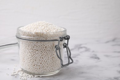 Photo of Tapioca pearls in jar on white marble table. Space for text