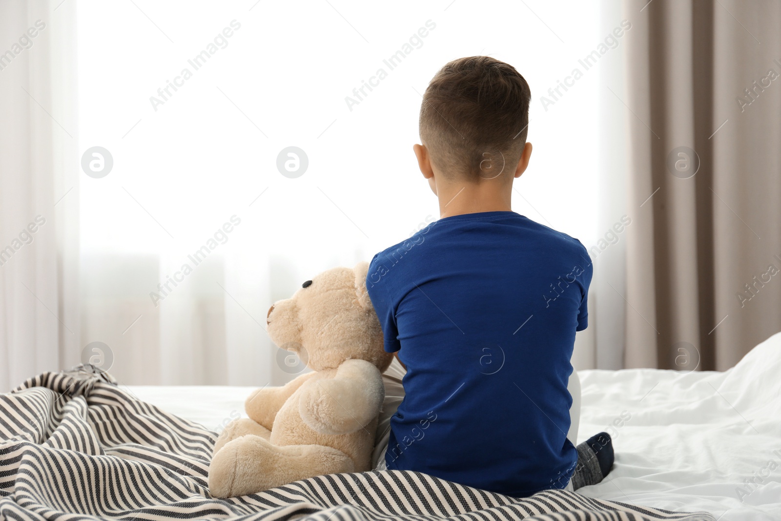 Photo of Lonely little boy sitting on bed in room. Autism concept