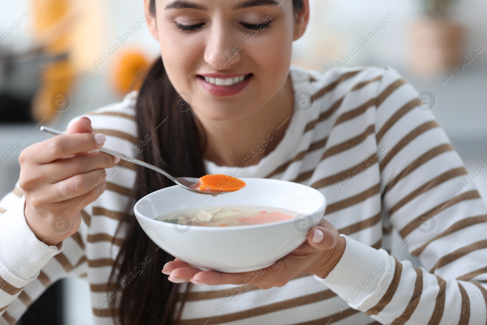 Photo of Young woman eating tasty vegetable soup indoors
