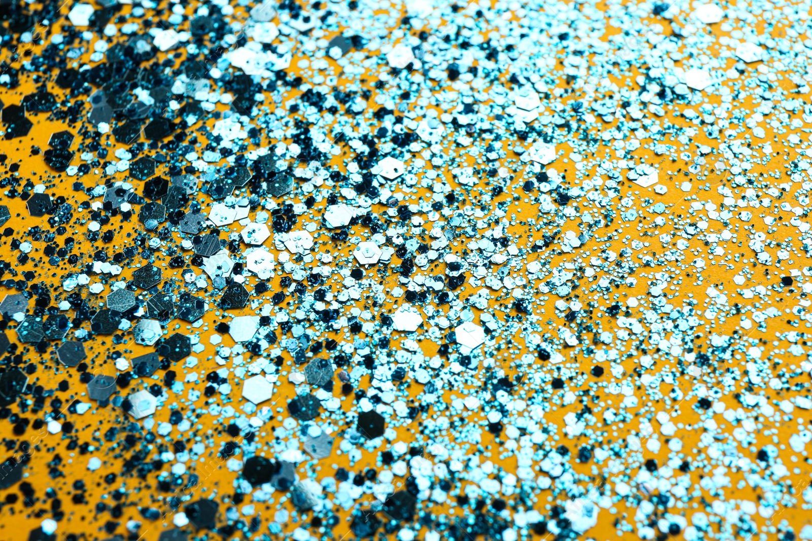 Photo of Shiny bright light blue glitter on yellow background, closeup